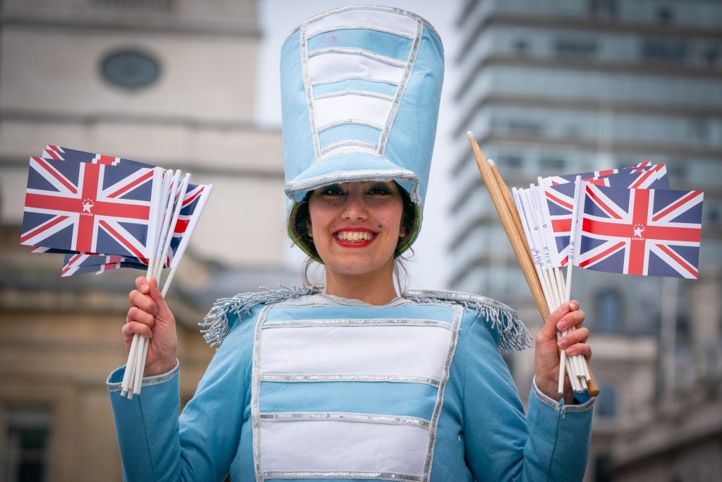 American Marching Band performer, smiling holding Great Britain flags at the London Parade.