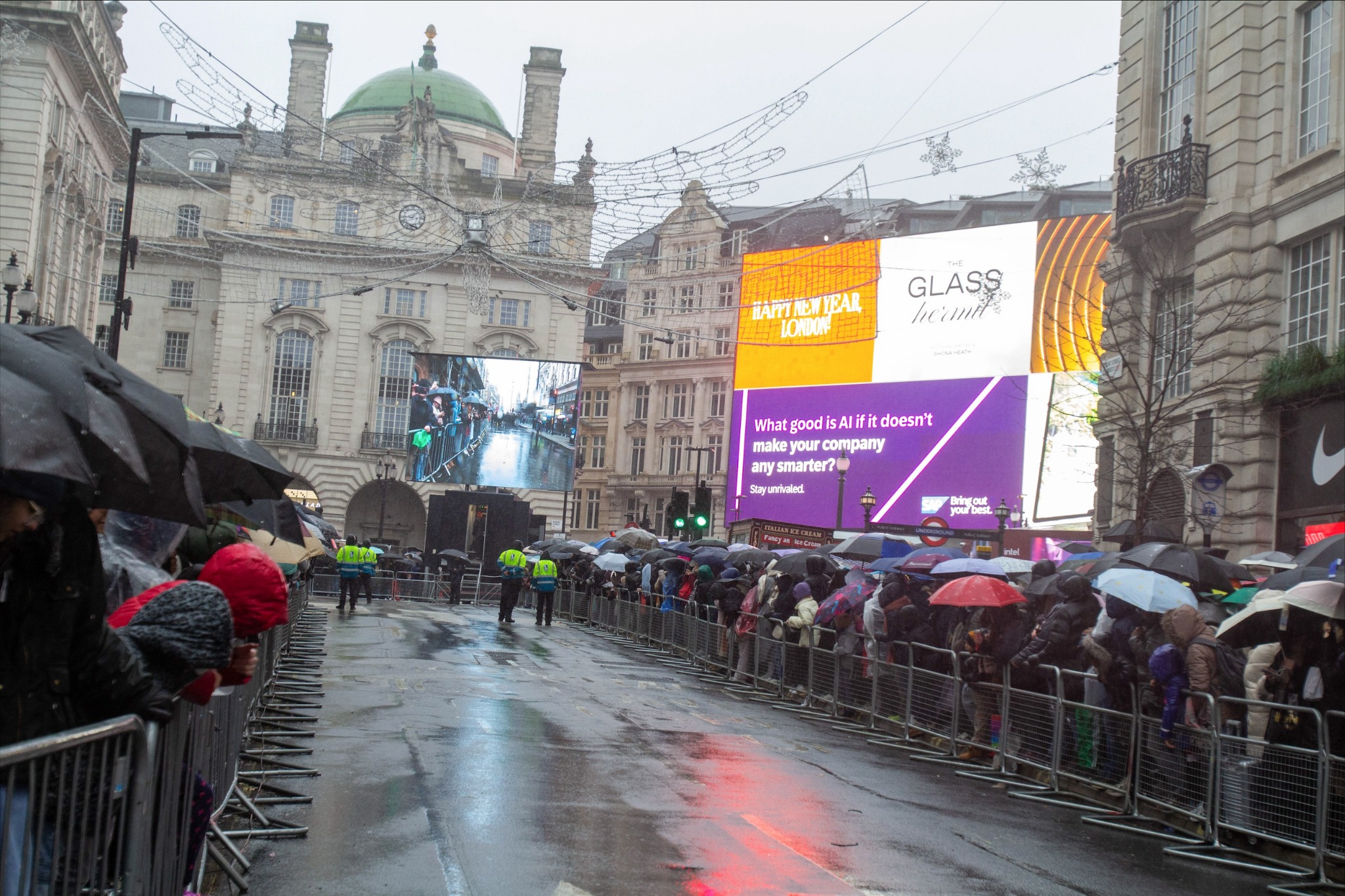 Rainy parade in Piccadilly Circus with crowds watching under umbrellas