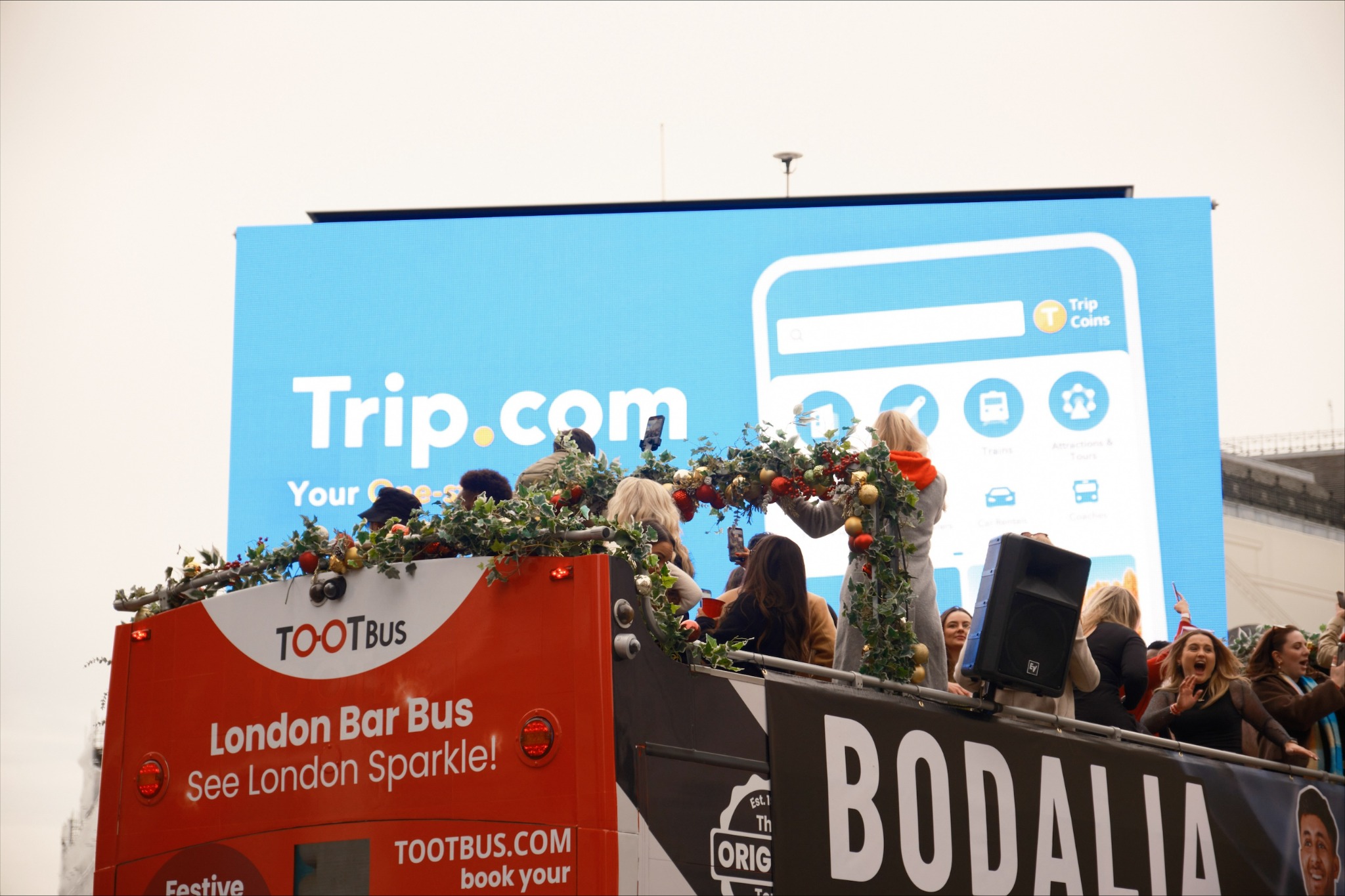 London Bar Bus festive tour with crowd and Trip.com billboard in Piccadilly Circus